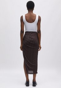 Bruin gestreepte midi-jurk met een slanke, gedrapeerde stijl, hoge split en doorschijnende textuur, gecombineerd met een aansluitend wit tanktop en zwarte schoenen.