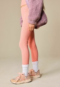 Leggings rosa a coste abbinati a una giacca lilla pelosa e sneakers con stampa animalier. Calzini bianchi a coste indossati sopra la caviglia.