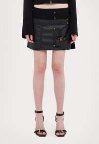 Svart minikjol i läder med gulddetaljer, med midja med knappar och en texturerad framfickdetalj.