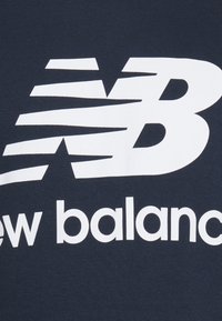 New Balancen logo, jossa valkoinen tyylitelty "NB" ja brändin nimi alla tummalla kangaspohjalla.