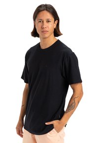 T-shirt nera a maniche corte in tessuto testurizzato, con scollo rotondo e piccolo dettaglio del logo sul petto. Design semplice.