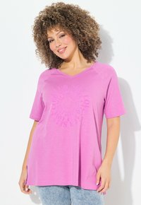 Camiseta rosa de manga corta con cuello en V y un diseño circular en relieve en la parte delantera. Hecha de una tela suave y ligera.