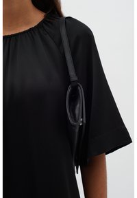 Černý top s krátkým rukávem a nabíraným výstřihem, doplněný malou černou koženou kabelkou s elegantním designem a ramenním popruhem.
