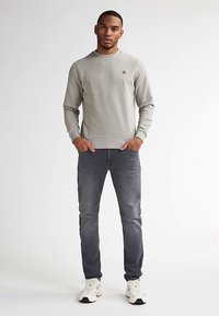 Šedá mikina s kulatým výstřihem a emblémem na prsou, doplněná tmavě šedými úzkými džínami a bílými teniskami.