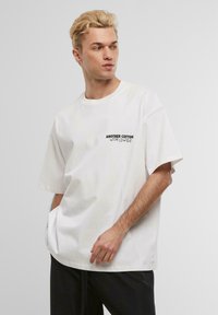 White cotton T-shirt with short sleeves, standard fit, featuring black "ANOTHER COTTON WORLDWIDE" text on the left chest area.