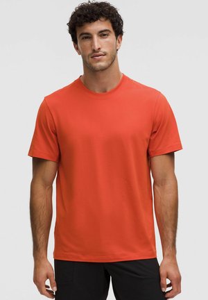 Kurzärmliges T-Shirt mit Rundhalsausschnitt in leuchtendem Orange, aus glattem, leichtem Stoff gefertigt, mit minimalen Nähten und einer lockeren Passform.