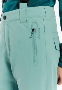 Jasnozielone wodoodporne spodnie z regulowanymi szelkami, z zamykaną na zamek kieszenią i przeszyciami. Gładka tekstura z dopasowanym krojem.