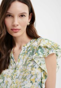 Bloemige blouse met ruches mouwen, met een pastelgeel, groen en wit patroon. Voorzijde met knopen en een lichte stofstructuur.