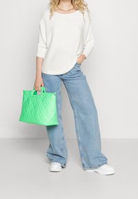 Grüne, gesteppten Tragetasche mit doppelten Griffen, aus glänzendem synthetischem Material. Kombiniert mit hellblauen, weiten Jeans und einem cremefarbenen Pullover.
