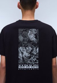 Black t-shirt featuring a white graphic design of intricate line patterns and the text "NAPAPIJRI geographic" at the bottom.
