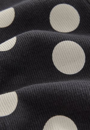 Schwarzer Stoff mit einer gerippten Textur, versehen mit großen, cremefarbenen Punkten, gleichmäßig verteilt. Der Stoff wirkt weich und flexibel.