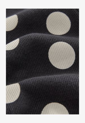 Črna tkanina z rebrasto teksturo, ki ima velike kremasto bele pikice, enakomerno razporejene. Tkanina se zdi mehka in prožna.