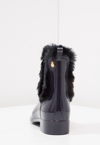 Black glossy ankle boot with faux fur trim, rounded toe, and a small gold accent on the side. Texture contrasts between smooth and soft.
