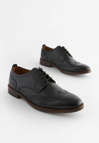 Black leather dress shoes with wingtip design, perforated detailing, and lace-up closure. Brown outsole provides contrast to the upper.