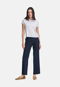 Vit t-shirt med kort ärm i kombination med navyblå vida byxor och bruna loafers, uppvisad mot en enkel bakgrund.