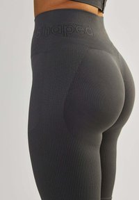 Donkergrijze high-waisted leggings met ribbelstructuur, voorzien van een 'shaped' logo op de tailleband en een gladde paneling aan de achterkant.