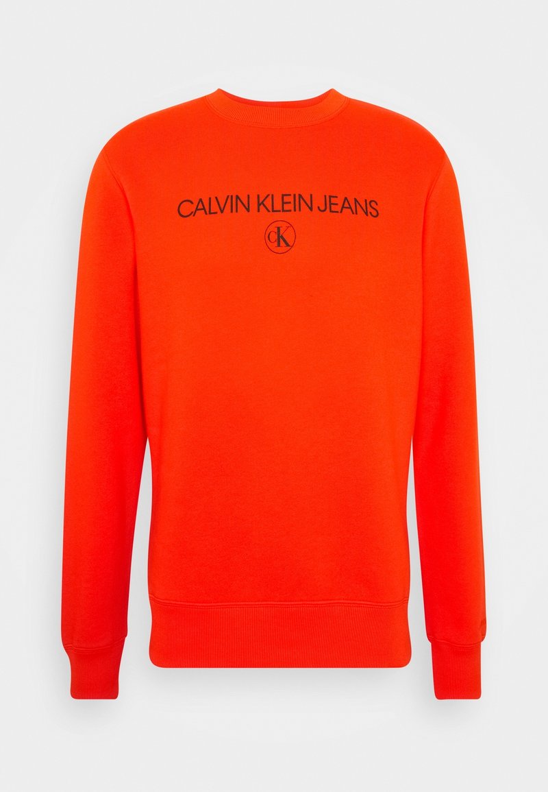 Sweatshirt à manches longues orange vif avec poignets et ourlet côtelés, arborant le texte « CALVIN KLEIN JEANS » et le logo circulaire « ck » en noir sur la poitrine.