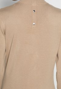 Maglione beige a maniche lunghe con finitura testurizzata, caratterizzato da uno spacco posteriore con due bottoni metallici e un colletto a coste.