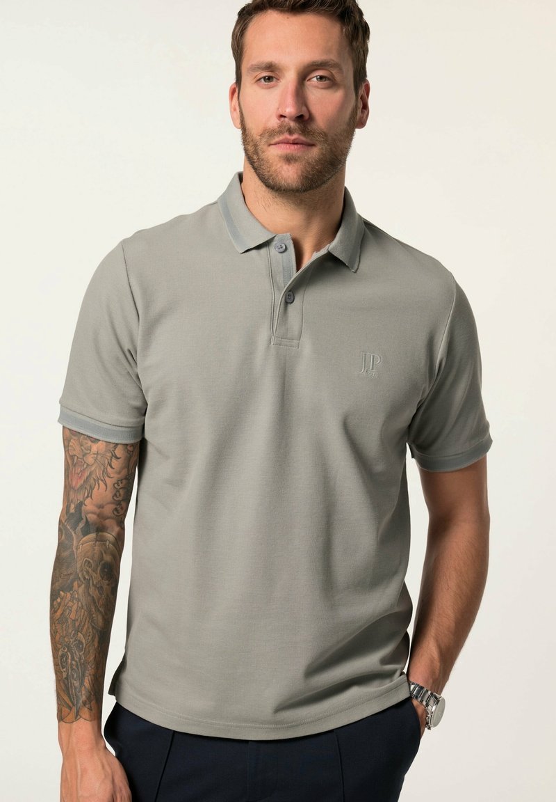 Camisa polo gris con tejido texturizado, mangas cortas y una tapeta de dos botones. Presenta un cuello de color contrastante más oscuro y un sutil logo.