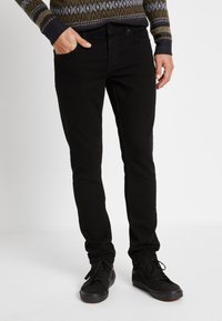 Jeans negros de corte slim, con un diseño clásico de cinco bolsillos y costuras sutiles. Llevados con zapatillas negras para un look cohesivo.