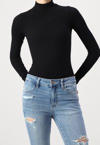 Černý žebrovaný rolák spárovaný s světle modrými roztrhanými džíny s trhanými detaily a knoflíkovým zapínáním. Hladký povrch látky.