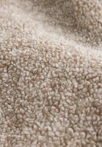 Teksturowana beżowa tkanina o miękkiej, puszystej powierzchni, prezentująca kręcony, pętliasty wzór i aksamitny wygląd.