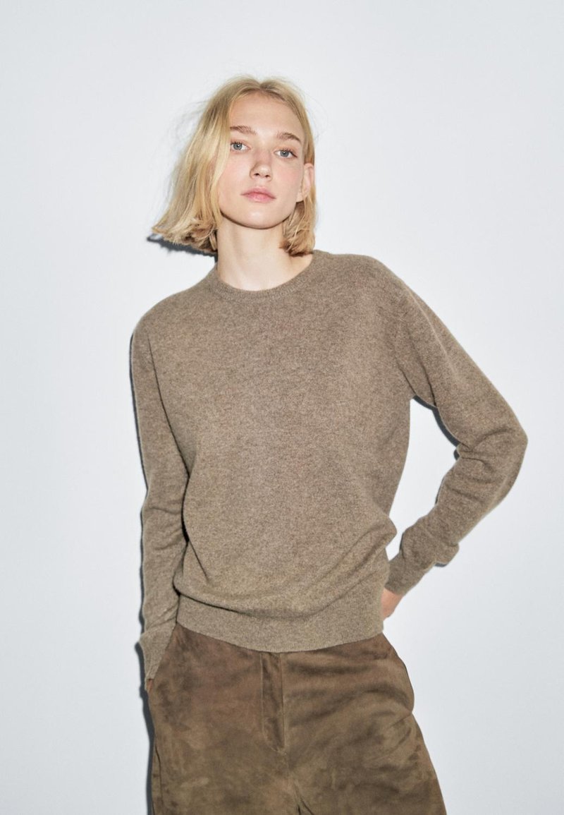 Maglione in lana marrone con collo tondo e maniche lunghe, abbinato a pantaloni scamosciati marrone scuro. Texture morbida, vestibilità rilassata. Design semplice.