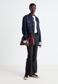 Denim jacket, white t-shirt, striped wide-leg pants, and black sneakers with cream accents. Holding a burgundy handbag.