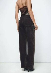 Pantalones anchos de pana marrón con bolsillos traseros. Textura suave y diseño de cintura alta. Combinados con un top de satén oscuro tipo camisola.