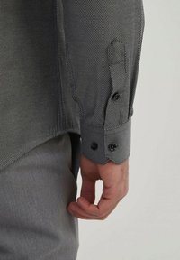 Chemise grise à motifs avec un gros plan sur un poignet à bouton noir. Le tissu a un tissage texturé, avec deux boutons visibles sur la manche.