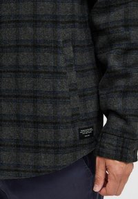 Grijs en zwart geruit shirt in een wolmix, met blauwe accenten, een omgeslagen kraag en een merklabel nabij de zoom aan de onderzijde rechts.