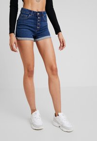 Denimshorts med hög midja, knappslå, uppvikta muddar och två framfickor. Mörkblå färg med subtila blekningar och sömnadsdetaljer.