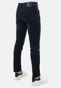 Donkerdenim jeans met een slim fit, voorzien van achterzakken, een leren merkpatch op de taille en een eenvoudige uitstraling. Gecombineerd met witte sneakers.