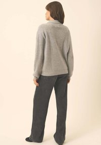 Grauer Strickpullover mit lockerer Passform, langen Ärmeln und gerippten Bündchen, kombiniert mit hoch sitzenden, dunkelgrauen, weiten Hosen.