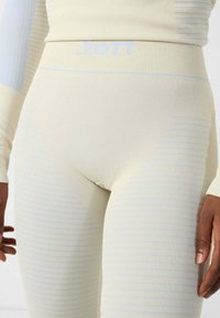 Leggings de color beige claro con textura acanalada y sutiles rayas horizontales azules. La cintura presenta el nombre de la marca en relieve en azul claro.