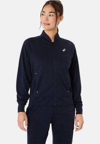 Jūrinės jėgos zip-up sportinė striukė, pagaminta iš lygaus audinio, su aukštu apykakle, priekinėmis kišenėmis ir mažuoju logotipu ant krūtinės.