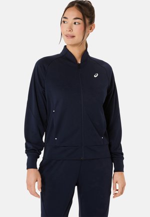 Marine blauwe sportjack met rits, gemaakt van gladde stof, voorzien van een hoge kraag, voorzakken en een klein logo op de borst.