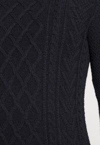 Pull en maille torsadée bleu marine présentant des motifs texturés avec des dessins en diamant et des torsades, mettant en valeur une finition en tissu doux.