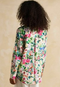 Blusa con estampado floral realizada en tela ligera, con vibrantes flores en rosa, azul y verde, mangas largas y un corte holgado.