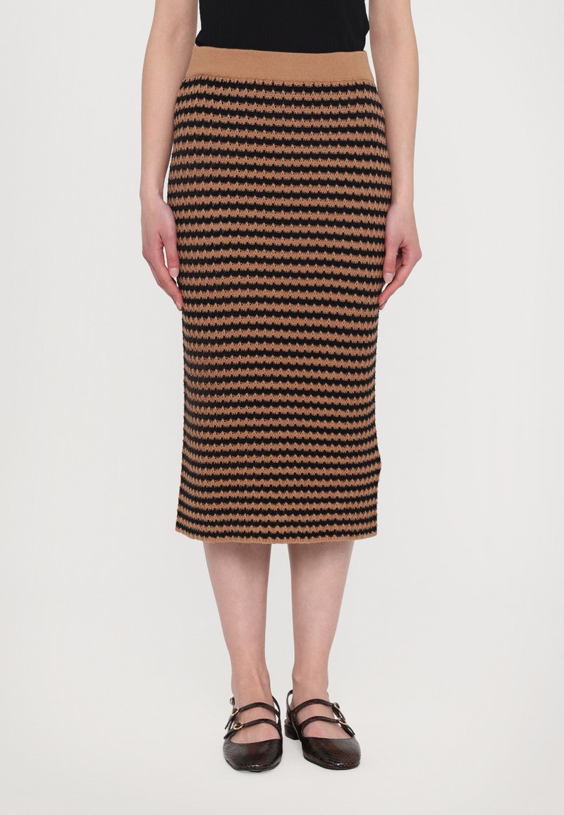 Pletená midi sukně v hnědé a černé barvě s vlnitým vzorem, disponující žebrovaným pasem a slim fit střihem. V kombinaci s černými Mary Jane botami.