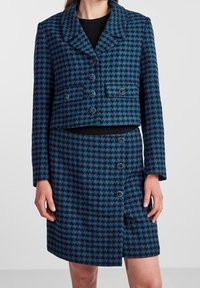 Zkrácená modro-černá houndstooth check sako s odpovídající sukní, které má kovové knoflíky a texturovanou látku.