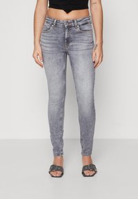 Világoskék, koptatott farmerből készült skinny farmernadrág, öt zsebbel és elöl gombos záródással. Fekete crop top-pal és szürke szandállal kombinálva.
