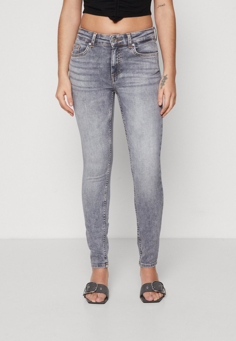 Világoskék, koptatott farmerből készült skinny farmernadrág, öt zsebbel és elöl gombos záródással. Fekete crop top-pal és szürke szandállal kombinálva.