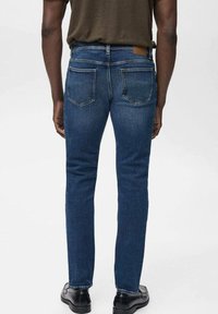 Jeans de denim azul oscuro con un corte ajustado, que presentan una cintura de altura media, bolsillos traseros y una etiqueta de cuero en la cinturilla. Textura suave.
