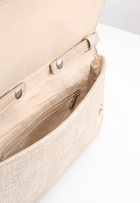 Interior de bolso beige con textura suave, que cuenta con un bolsillo con cremallera y cierre de botón. Forrado con tela beige más clara.