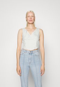 Top branco corto com decote em V e detalhe de franzido, combinado com jeans azul claro de cintura alta com costura vertical. Design simples.