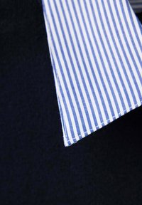 Col de chemise à rayures verticales bleues et blanches sur un pull bleu marine foncé.