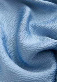 Jasnoniebieska tkanina o fakturze z tkanym wzorem, z delikatnymi fałdami i gładką powierzchnią, tworząca łagodne załamania i cienie.