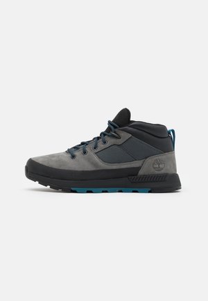Chaussure de randonnée mi-haute grise et noire avec des touches bleues, des panneaux en tissu texturé et une semelle en caoutchouc avec le logo Timberland au talon.