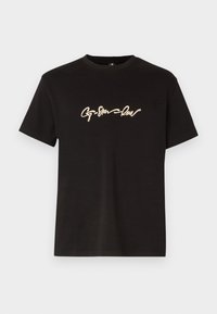 T-shirt en coton noir avec des manches courtes et un col rond. Design en script doré notable sur la poitrine. Coupe simple et moderne.